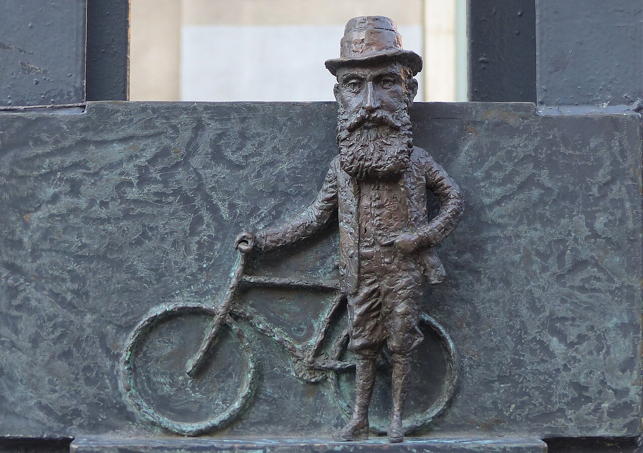 Theodor Herzl by Mihály Kolodko (2018 bronze statuette). The statuette placed on the light pole depicts Tivadar Herzl wth a bicycle.- at corner of Doh