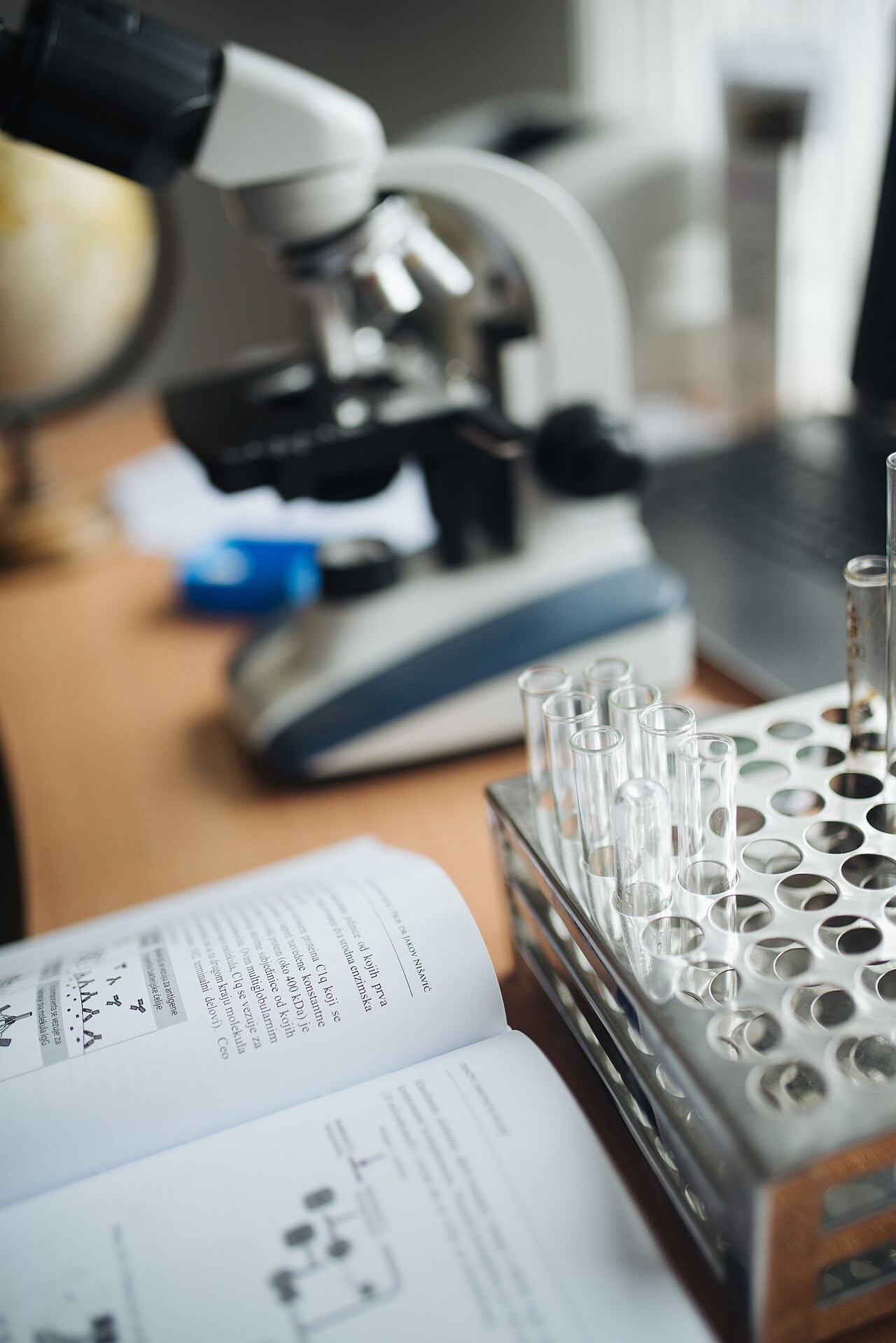 Close-up of a test tube rack in front of a chemistry book with microscope in a blurry background